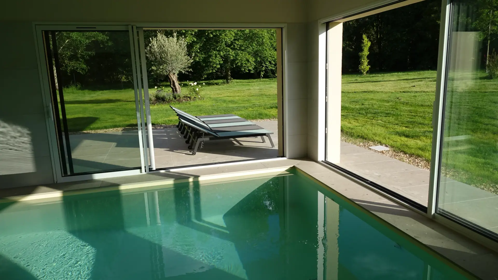 La piscine intérieure, baies vitrées ouvertes sur le jardin